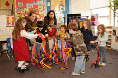 Children and adults gathered in a classroom holding colorful ribbon streamers.