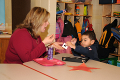 An adult and a child working together with small materials at a table.